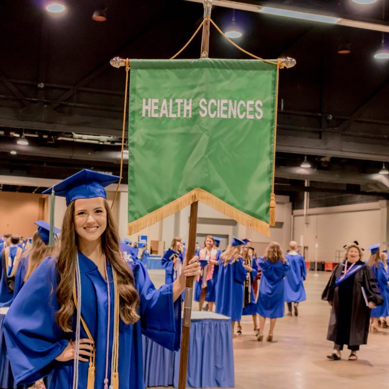 Students in cap and gown holding a Health Sciences flag